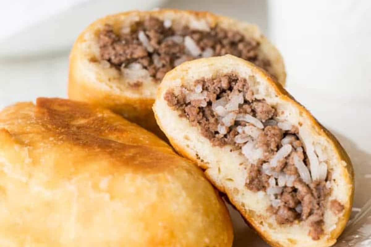 Close-up of two fried meat pies filled with ground beef and rice, with one pastry cut open to show the hearty filling.