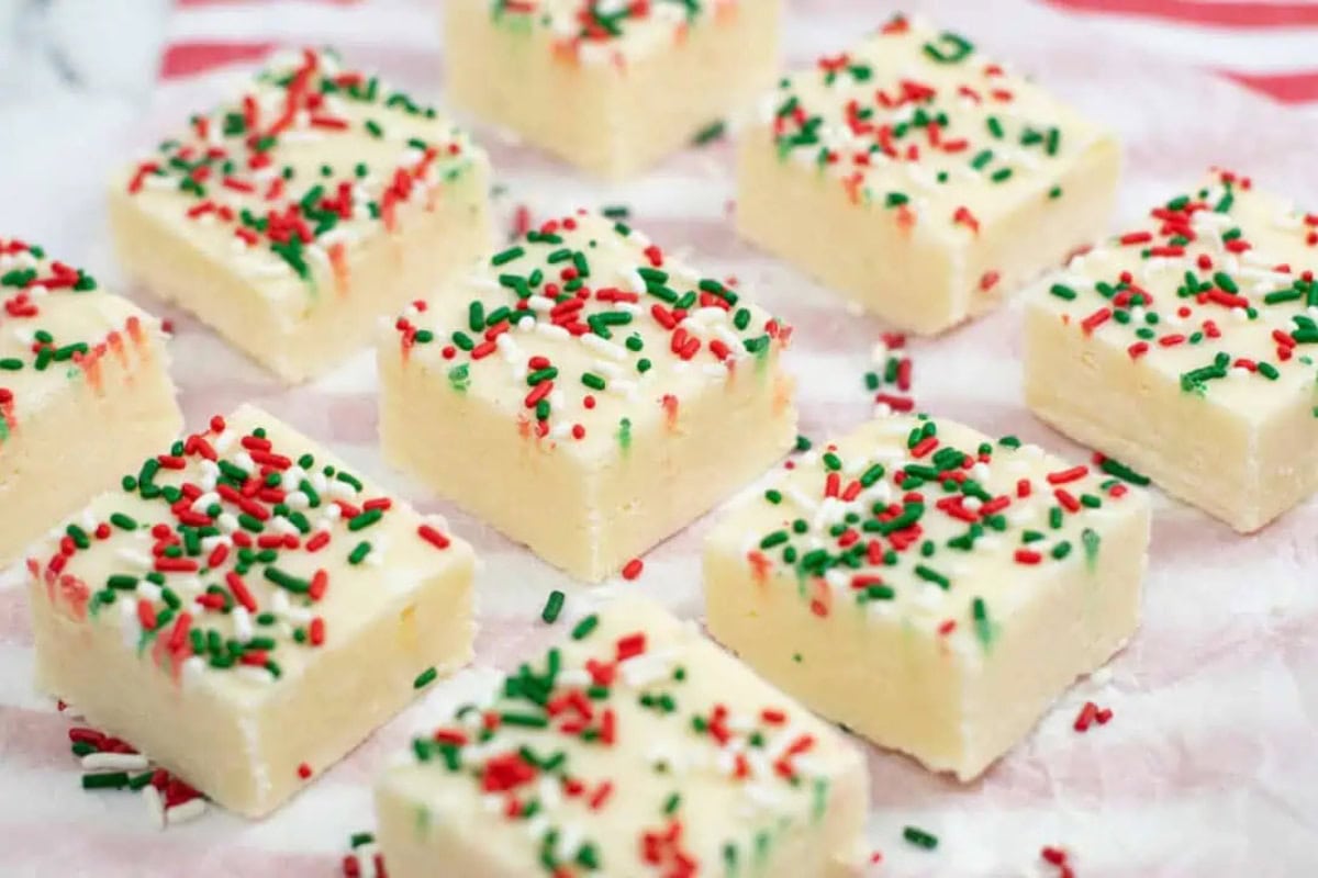 Squares of sugar cookie fudge topped with festive red and green sprinkles are arranged on parchment paper.