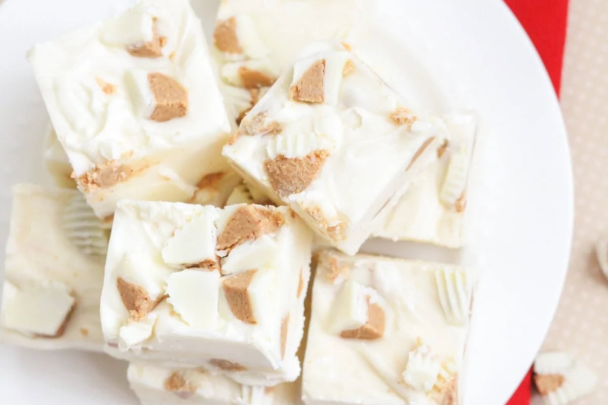 Fudge squares made with white chocolate and chunks of white peanut butter cups on a white plate, viewed from above.