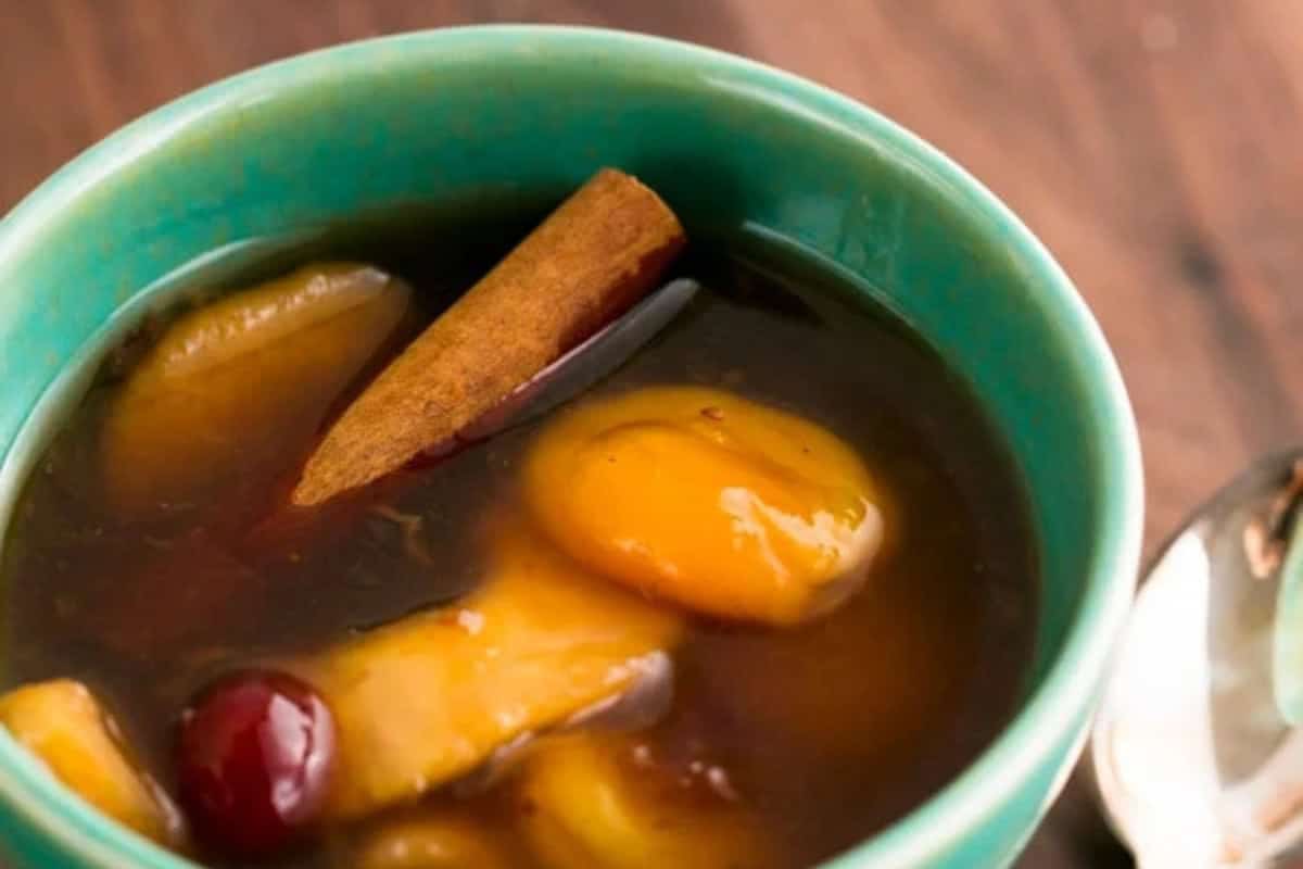 A bowl of kissel, a dried fruit soup, with whole fruits and a cinnamon stick in a thick syrup with a spoon on the side