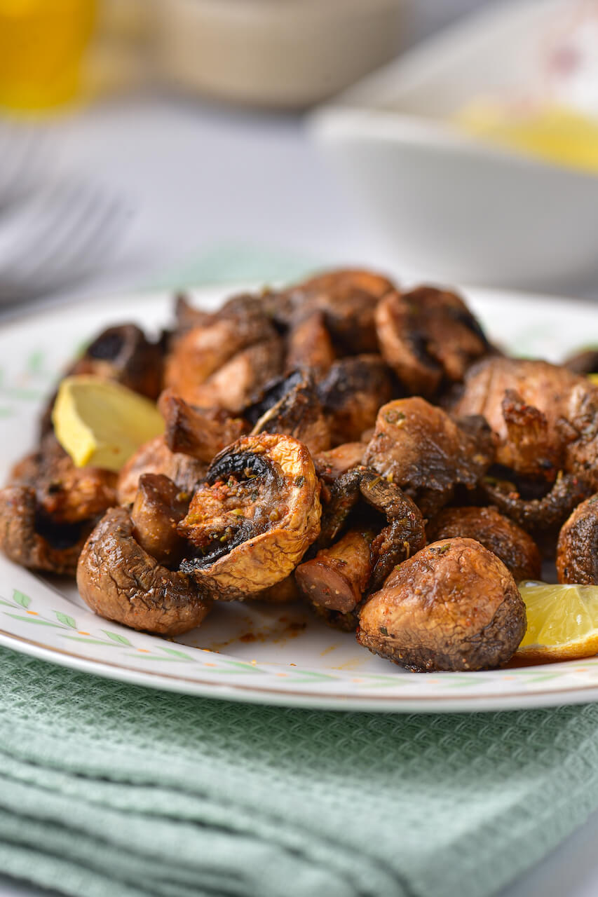 A white plate of air fryer mushrooms with lemon slices.