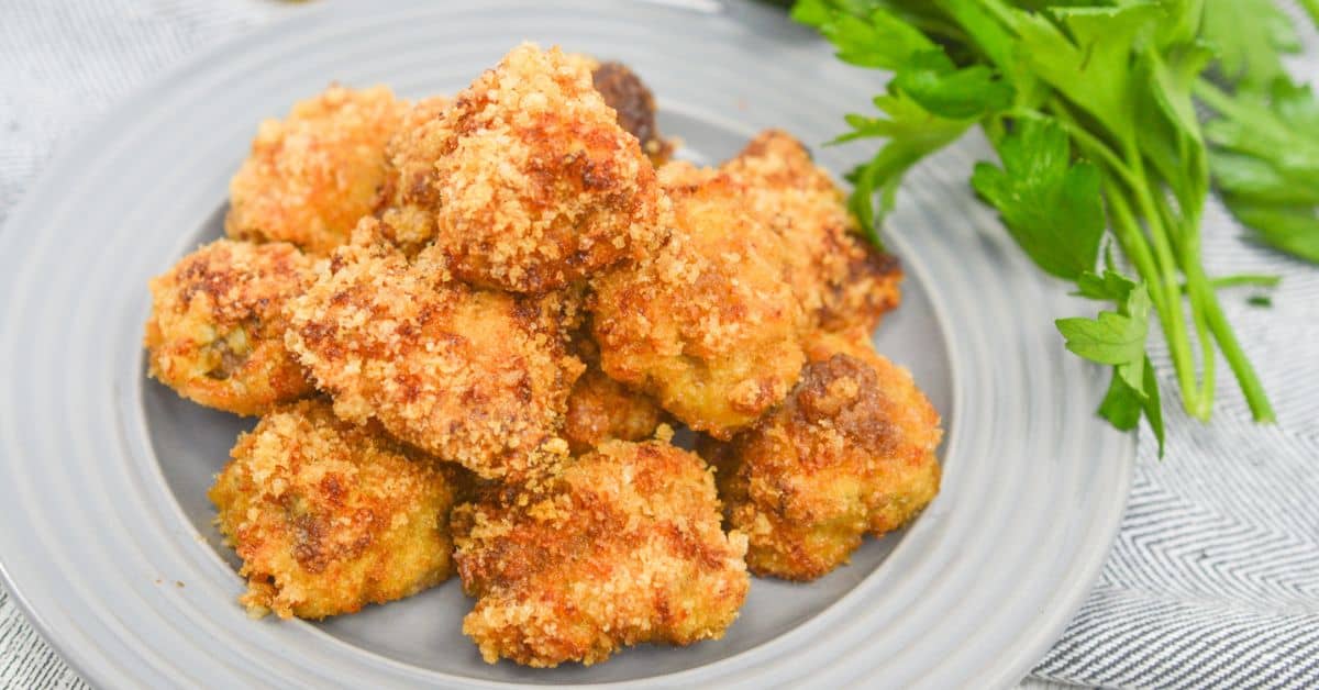 A plate of golden-brown breaded chicken nuggets sits next to a bunch of fresh parsley on a gray plate, making for a delicious pairing alongside your favorite Air Fryer Steak Bites.