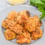 A plate of breaded, golden-brown meat with a small bowl of dipping sauce and fresh parsley on the side sits next to perfectly cooked for a delicious and satisfying meal.