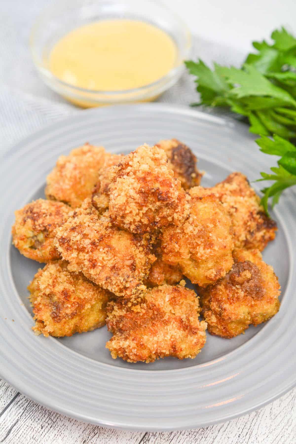 A plate of breaded, golden-brown meat with a small bowl of dipping sauce and fresh parsley on the side sits next to perfectly cooked  for a delicious and satisfying meal.