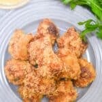 A gray plate with several pieces of breaded, baked nuggets next to a bunch of fresh parsley and a small bowl of dipping sauce—perfect alongside crispy Air Fryer Steak Bites for a delicious and easy meal.