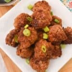 A plate of Asian Pork Meatballs garnished with chopped green onions, served on a white square dish on a wooden surface.