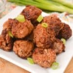 A plate of Asian Pork Meatballs garnished with sliced green onions, with fresh green onions in the background.