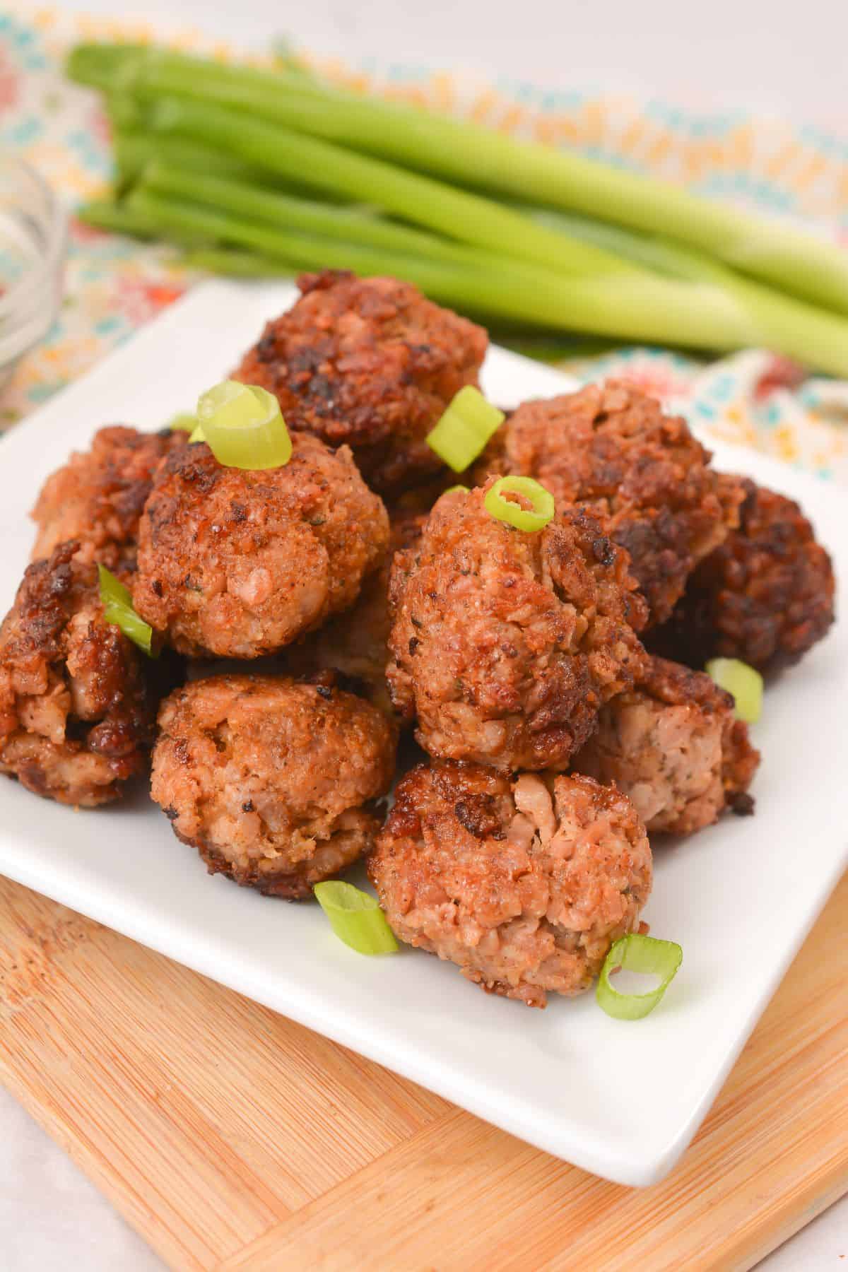 A plate of Asian Pork Meatballs garnished with chopped green onions, placed on a wooden board with fresh green onions in the background.