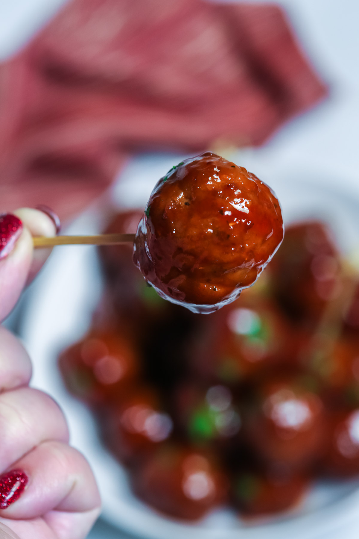 A person holding a barbecue and grape jelly meatball on a toothpick.