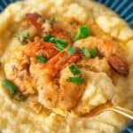 A plate of creamy grits topped with Cajun Shrimp and Grits, garnished with sautéed shrimp and chopped green onions, with a spoon lifting a portion.