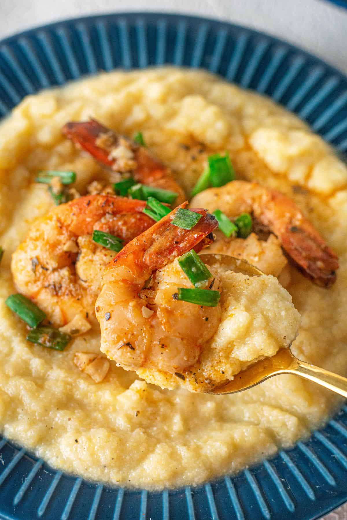 A plate of creamy grits topped with Cajun Shrimp and Grits, garnished with sautéed shrimp and chopped green onions, with a spoon lifting a portion.