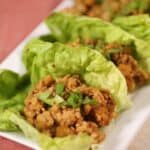 Three Asian Lettuce Wraps filled with seasoned ground meat and chopped vegetables, arranged on a white rectangular plate.