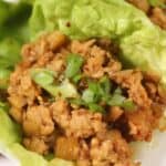 A close-up of Asian Lettuce Wraps featuring seasoned ground chicken and chopped vegetables served in fresh lettuce cups, garnished with sliced green onions.