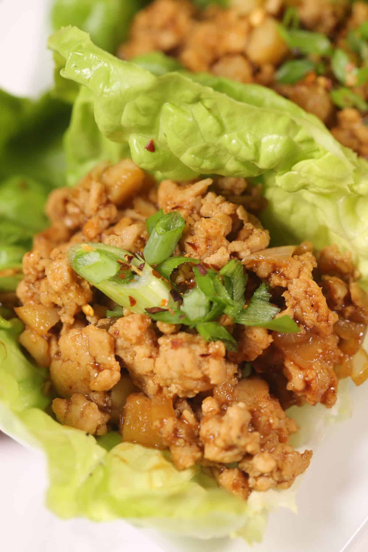 A close-up of Asian Lettuce Wraps featuring seasoned ground chicken and chopped vegetables served in fresh lettuce cups, garnished with sliced green onions.