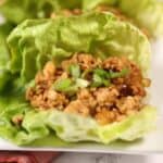 Three leaves filled with seasoned ground meat and garnished with chopped green onions are arranged on a white plate.