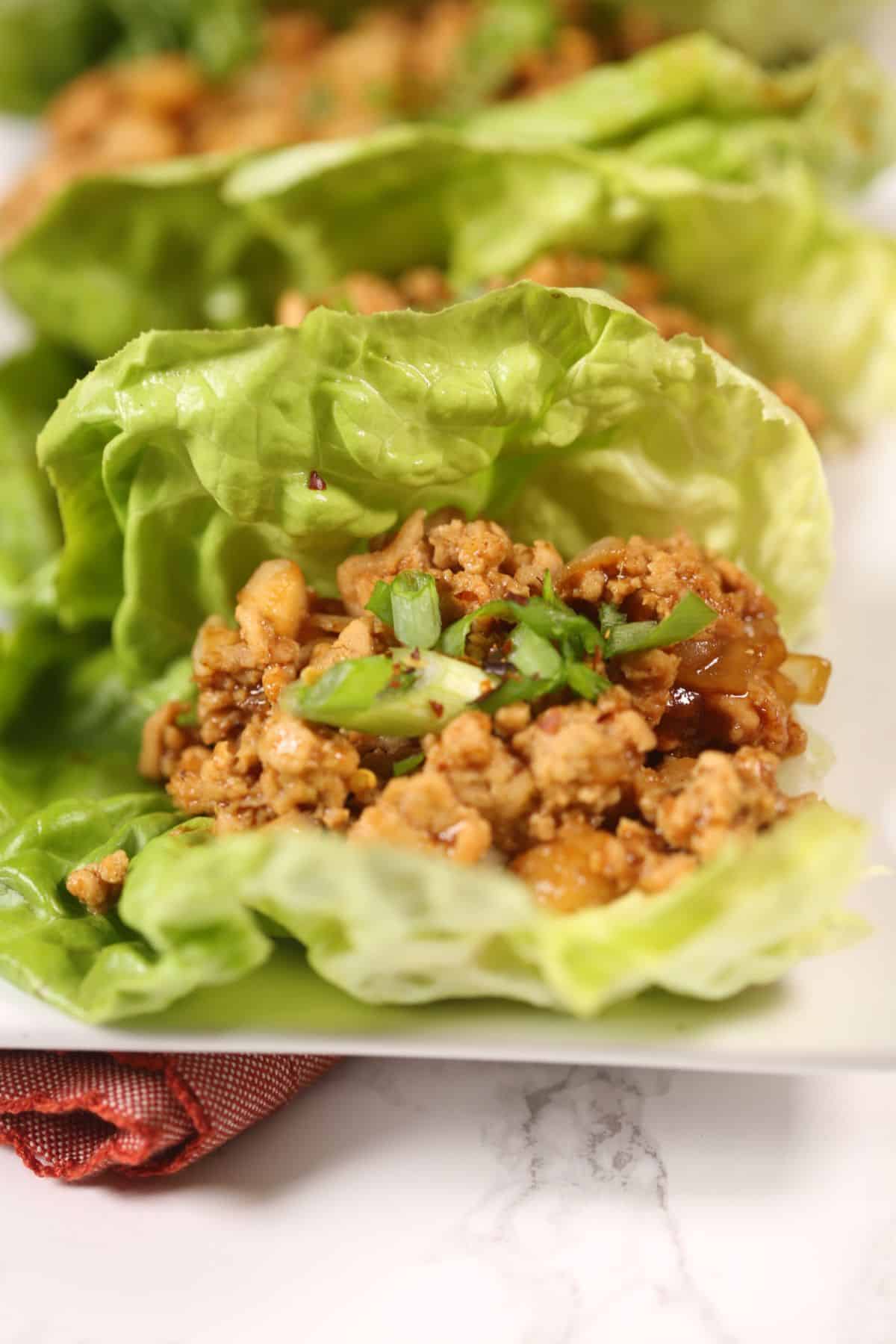 Three leaves filled with seasoned ground meat and garnished with chopped green onions are arranged on a white plate.