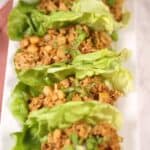 Four Asian Lettuce Wraps filled with seasoned ground meat, diced vegetables, and chopped green onions, arranged neatly on a white rectangular plate.