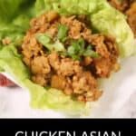 Two lettuce leaves filled with seasoned ground chicken and chopped vegetables, garnished with sliced green onions, serve as the perfect Asian Lettuce Wraps on a white plate.