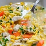 A bowl of Chicken Corn Noodle Soup with carrots, parsley, and tender pieces of chicken, with a spoon resting in the bowl.