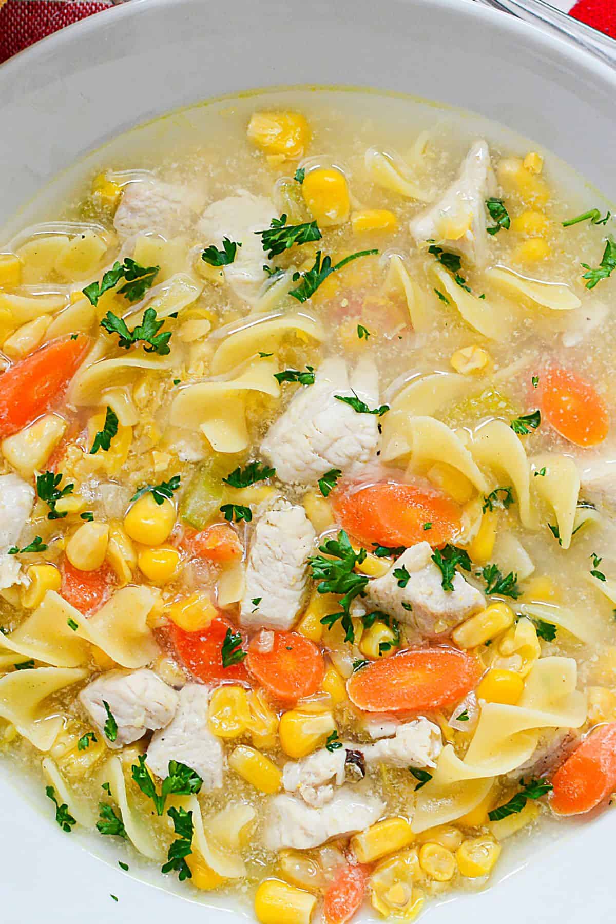 A close-up of a bowl with parsley, and chunks of meat in a clear broth.