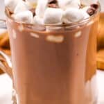 A glass mug , topped with mini marshmallows and a few chocolate chips.