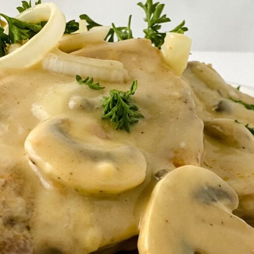 Close-up of a dish featuring juicy chicken covered in creamy mushroom sauce, reminiscent of Pork Chops with Mushrooms and Gravy, garnished with sliced mushrooms, onions, and fresh parsley.