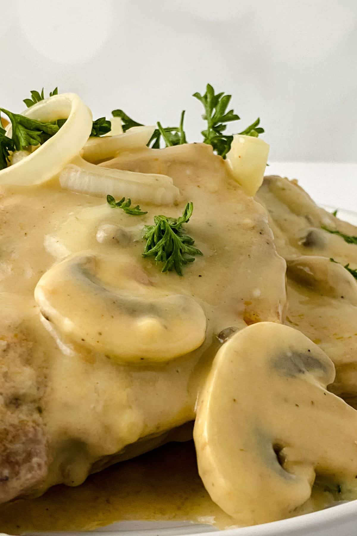 Close-up of a dish featuring juicy chicken covered in creamy mushroom sauce, reminiscent of Pork Chops with Mushrooms and Gravy, garnished with sliced mushrooms, onions, and fresh parsley.