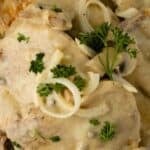 A plate of chicken covered in creamy mushroom sauce, garnished with fresh parsley and sliced onions—perfect for fans of Pork Chops with Mushrooms and Gravy.