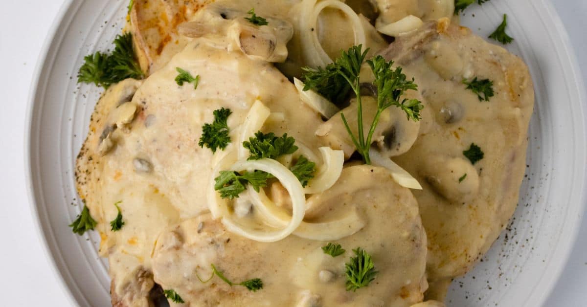 A plate of chicken covered in creamy mushroom sauce, garnished with fresh parsley and sliced onions—perfect for fans of Pork Chops with Mushrooms and Gravy.
