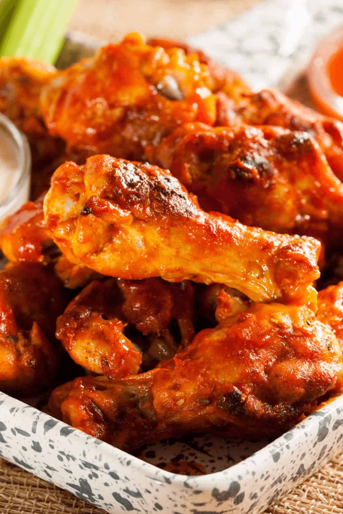 A pile of saucy Honey BBQ wings sits invitingly on a plate, accompanied by a small cup of dipping sauce in the background.