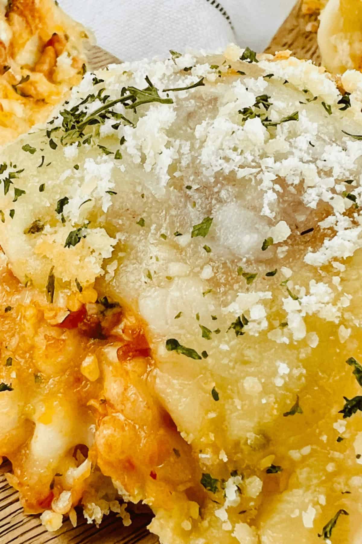 Close-up of a slice of cheese lasagna topped with grated cheese and herbs on a wooden board, exuding the same irresistible allure you'd find in a tray of meatball sliders.