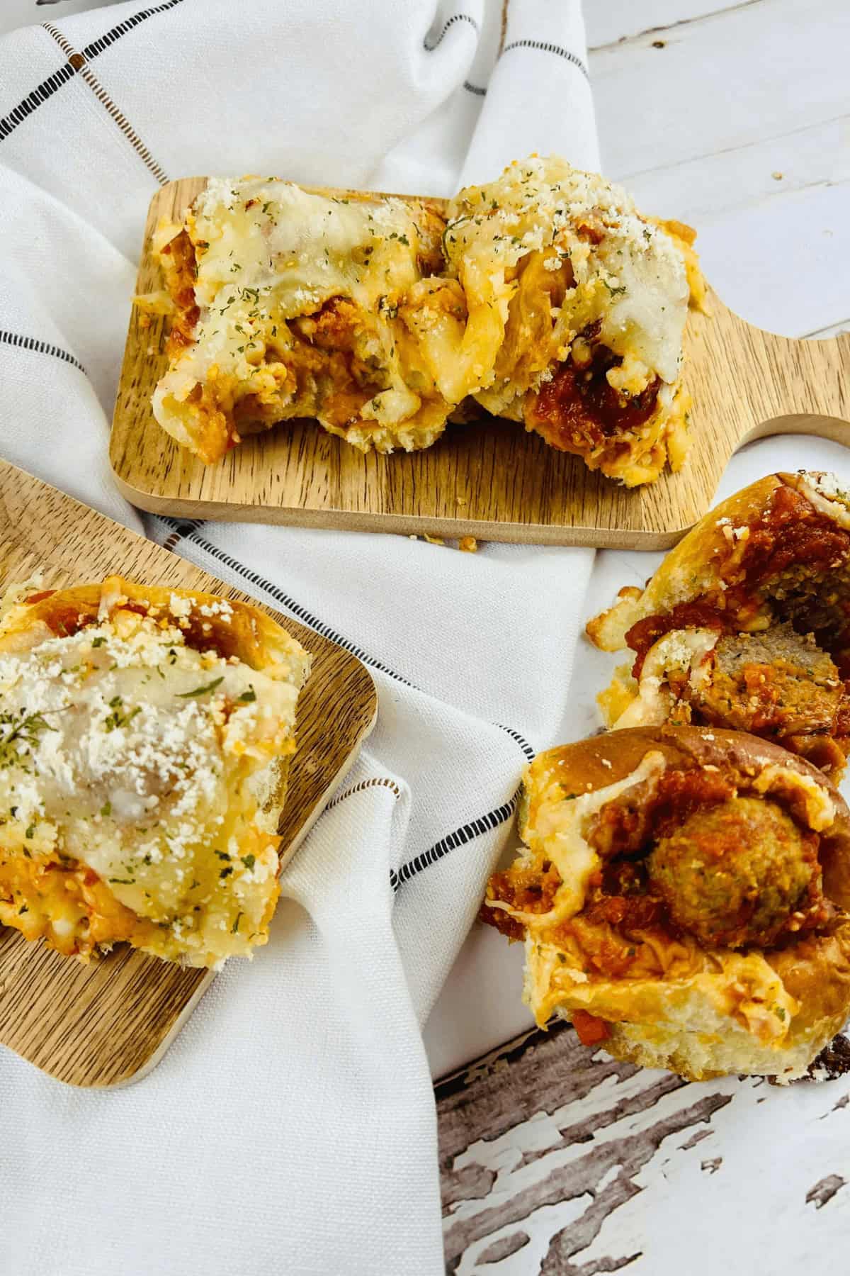 Meatball sliders nestled with sauce and cheese grace wooden boards, against a backdrop of white cloth.