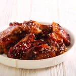 A plate of succulent Korean BBQ wings, glazed to perfection and topped with sesame seeds, sits invitingly on a rustic wooden table.