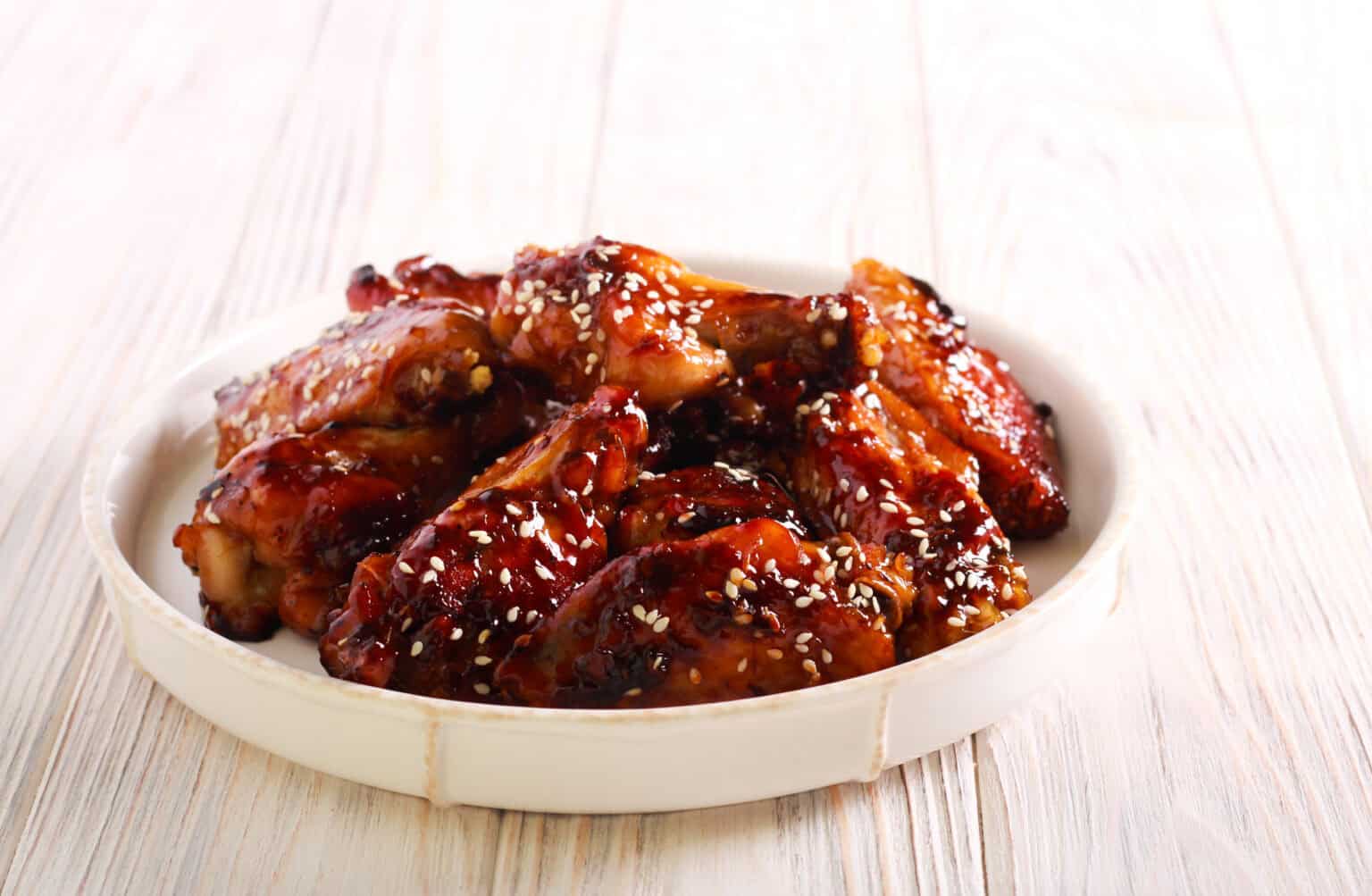 A plate of succulent Korean BBQ wings, glazed to perfection and topped with sesame seeds, sits invitingly on a rustic wooden table.