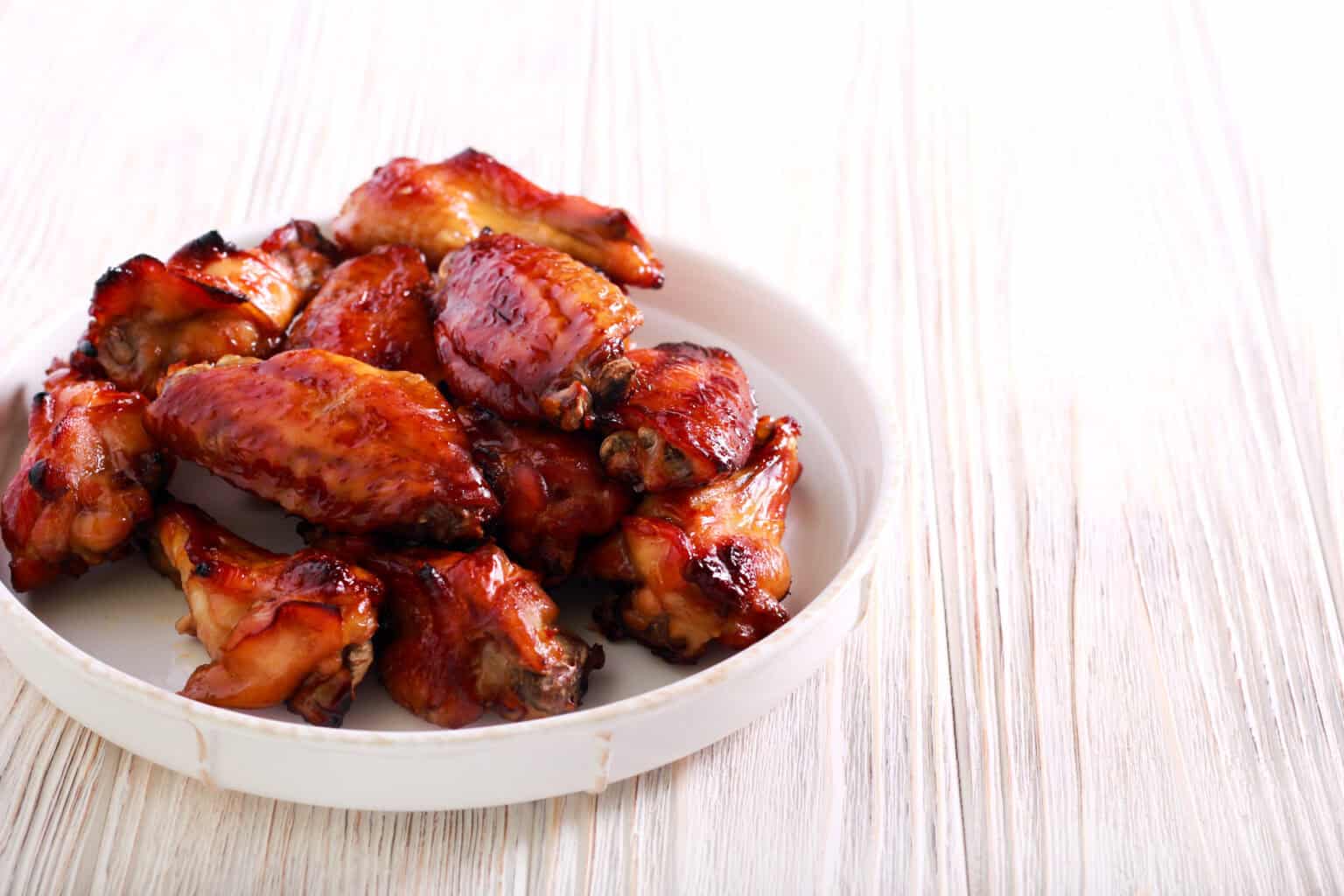 A plate of chicken  sits enticingly on a light wooden surface.