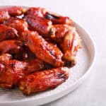 Plate of Korean BBQ wings, glazed to perfection, arranged in a tempting pile on a white plate, placed on a light-colored surface.