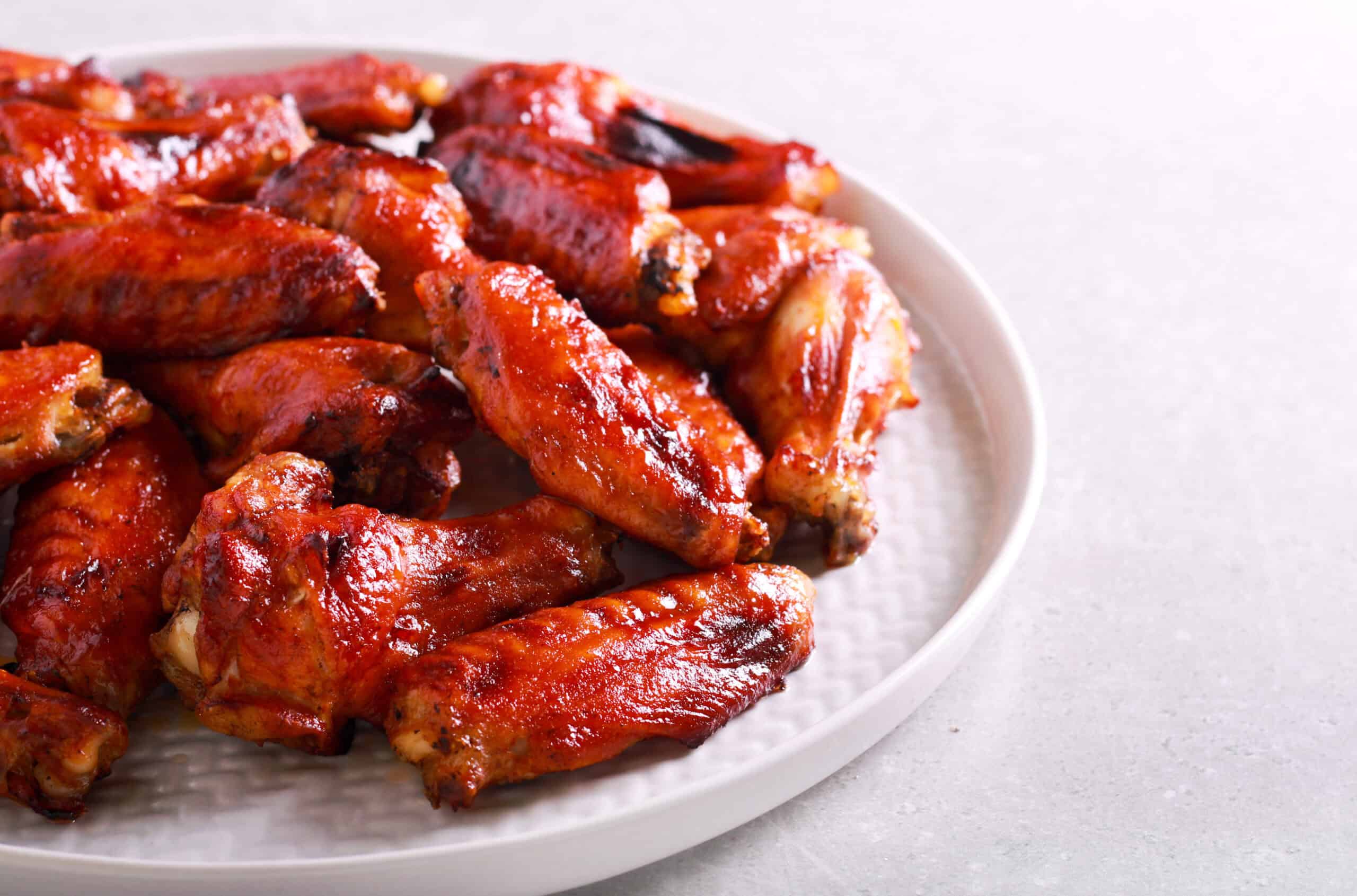 Plate of Korean BBQ wings, glazed to perfection, arranged in a tempting pile on a white plate, placed on a light-colored surface.