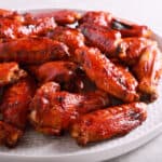 A white plate piled with Korean BBQ wings, glazed to perfection, showcasing a glossy, reddish-brown color.
