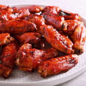 A white plate piled with Korean BBQ wings, glazed to perfection, showcasing a glossy, reddish-brown color.