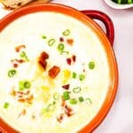 A bowl of creamy Lighter Corn Chowder topped with chopped green onions and bacon bits, served alongside sliced bread and a small bowl of fresh green onions.