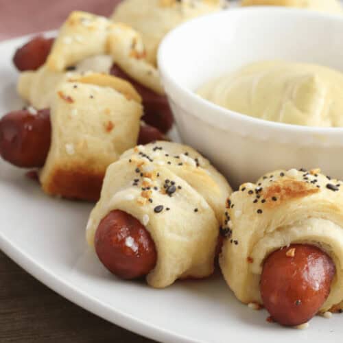 A plate of Little Smokies Pigs in a Blanket, perfectly complemented by a small bowl of tangy mustard dipping sauce.