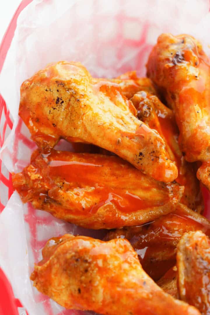 A basket of crispy, golden oven-baked buffalo wings coated in bright orange sauce sits invitingly on white paper.