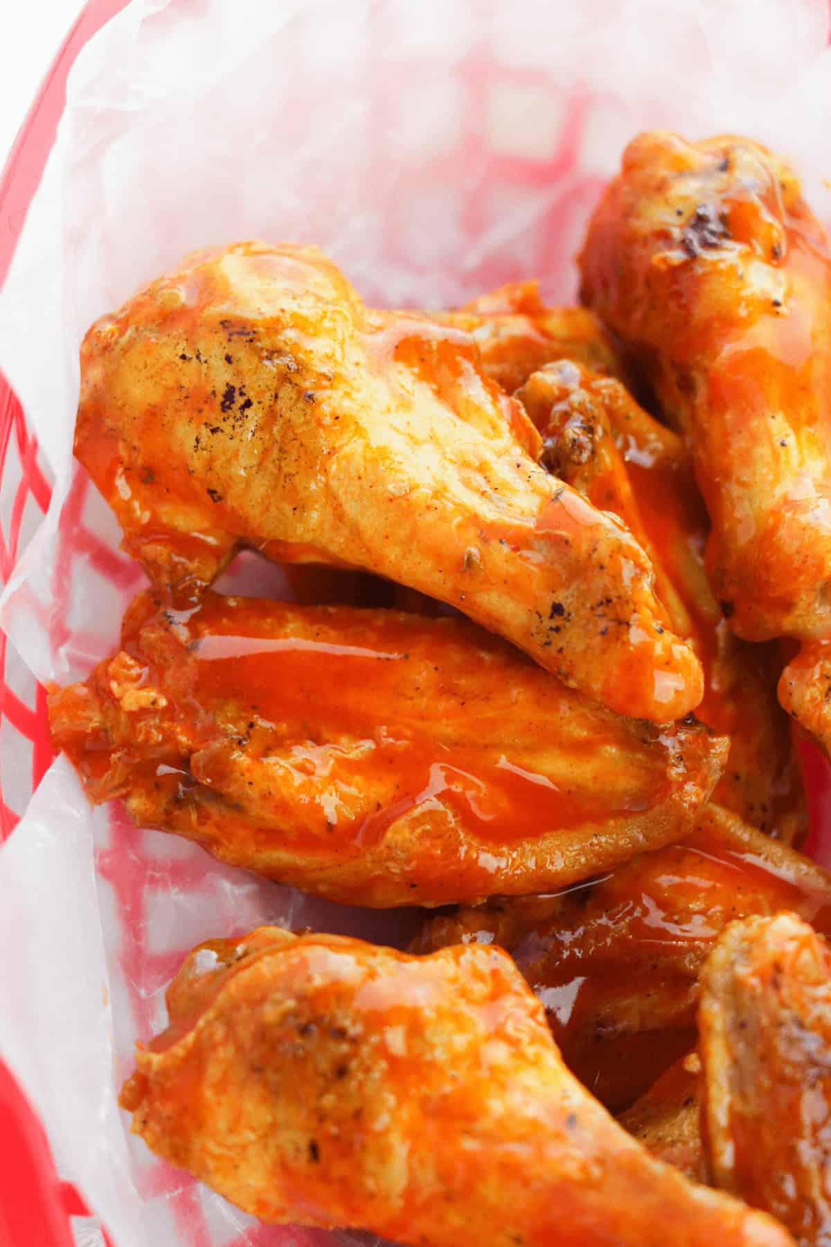A basket of crispy, golden oven-baked buffalo wings coated in bright orange sauce sits invitingly on white paper.