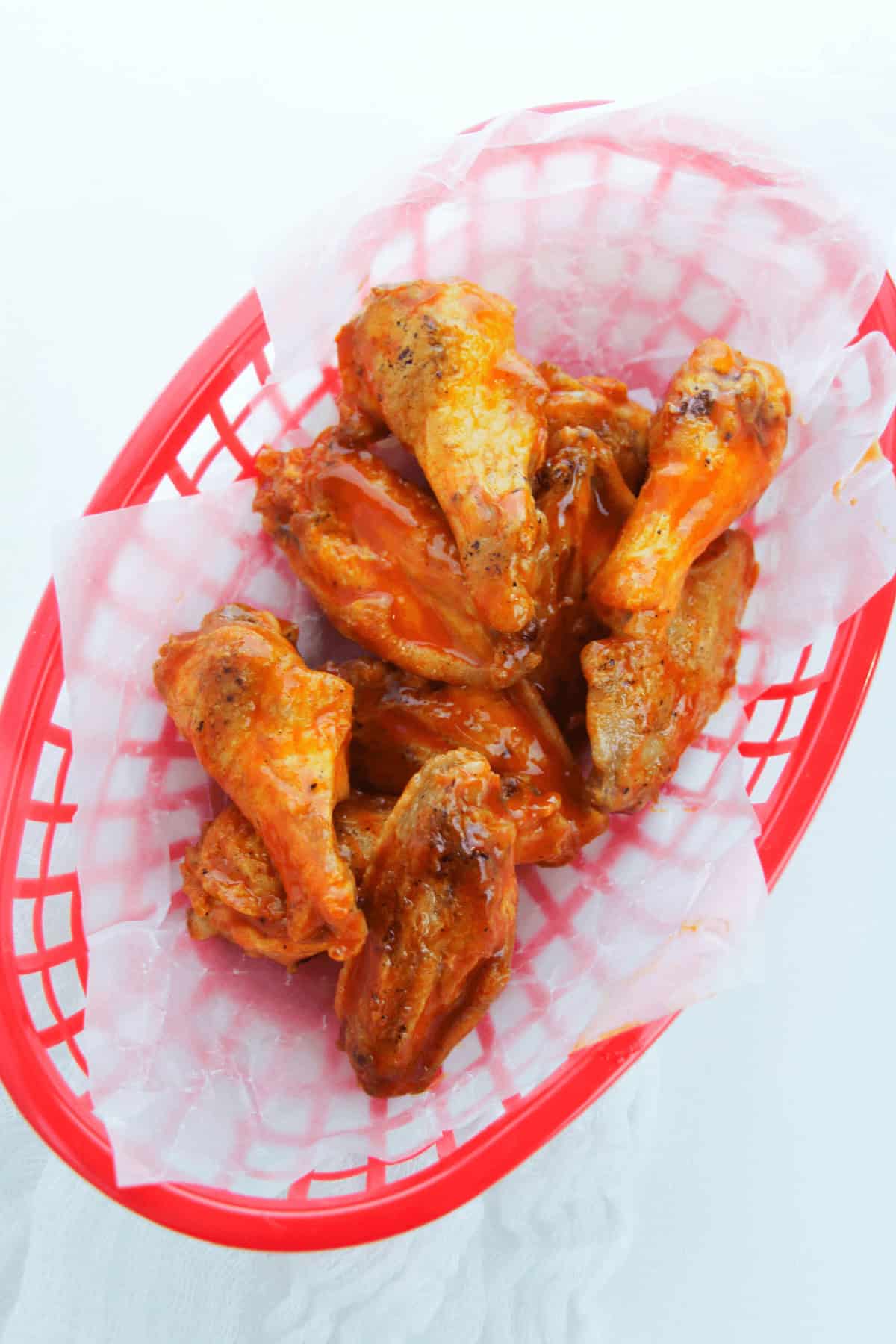 A red basket lined with paper holds several pieces of sauced oven-baked Buffalo wings.