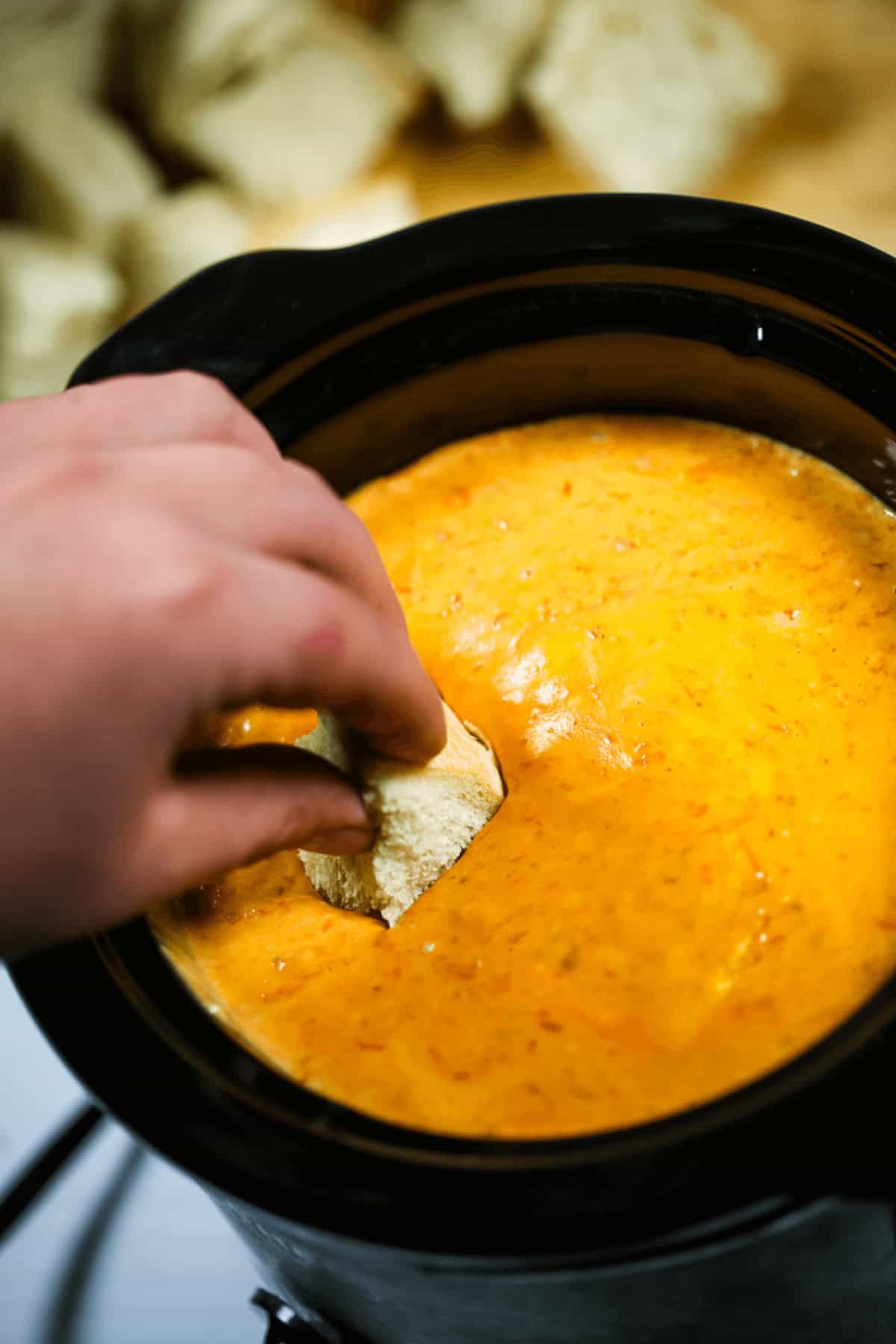 A hand dips a tortilla chip into a pot of melted slow cooker pizza dip.