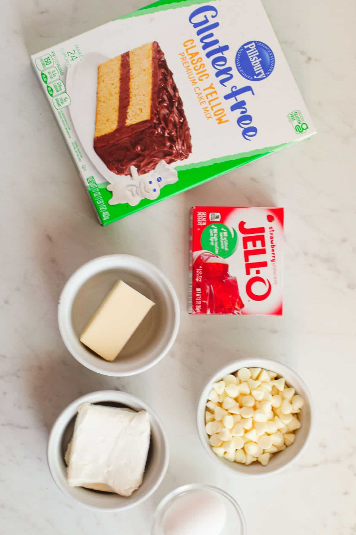 A tempting batch begins with gluten-free yellow cake mix, strawberry gelatin, butter, cream cheese, white chocolate chips, and an egg—artfully arranged on a marble surface.