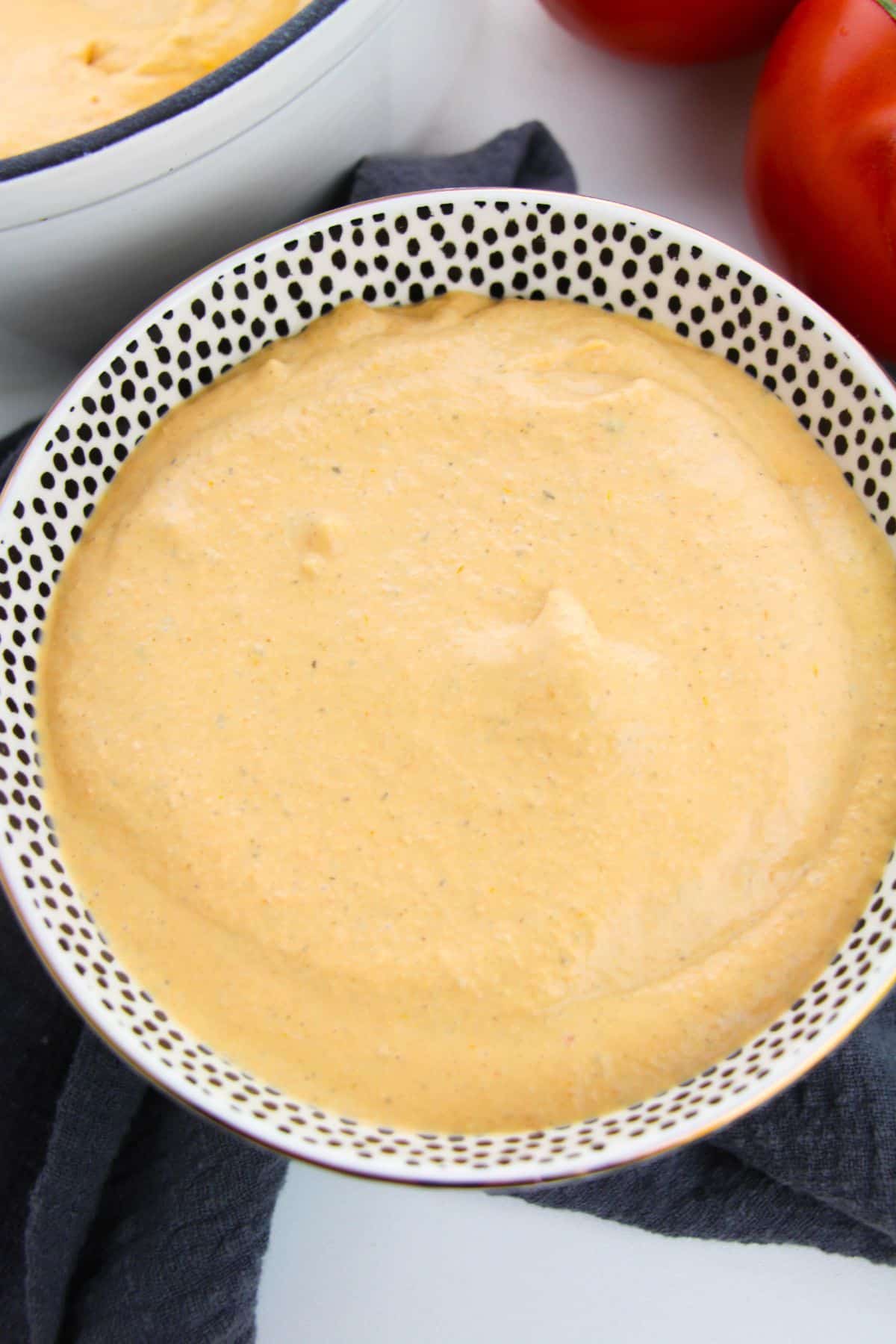A bowl filled with thick, creamy Tomato Basil Bisque sits on a dark cloth, with ripe tomatoes visible in the background.