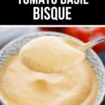 A spoonful of creamy Tomato Basil Bisque held above a bowl filled with the same soup, with fresh tomatoes in the background.