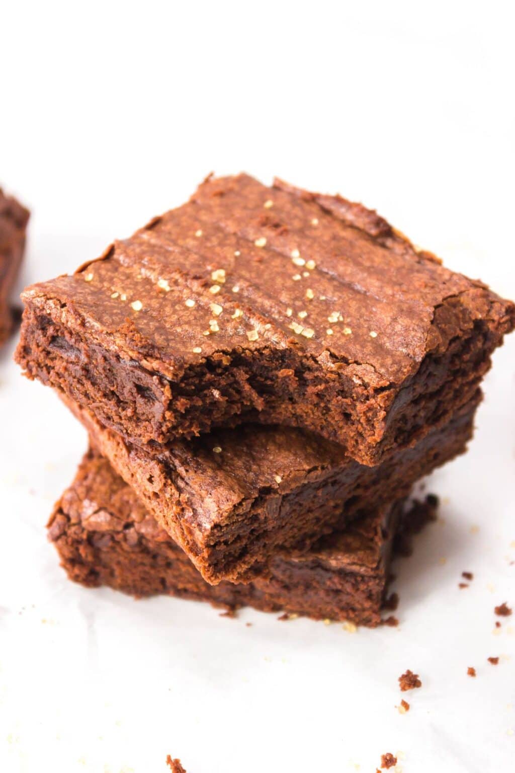 Two Triple Chocolate Brownies stacked on parchment paper, with a slightly cracked top and a sprinkle of golden sugar on the surface.