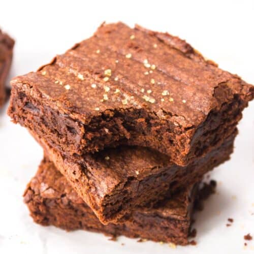Two Triple Chocolate Brownies stacked on parchment paper, with a slightly cracked top and a sprinkle of golden sugar on the surface.
